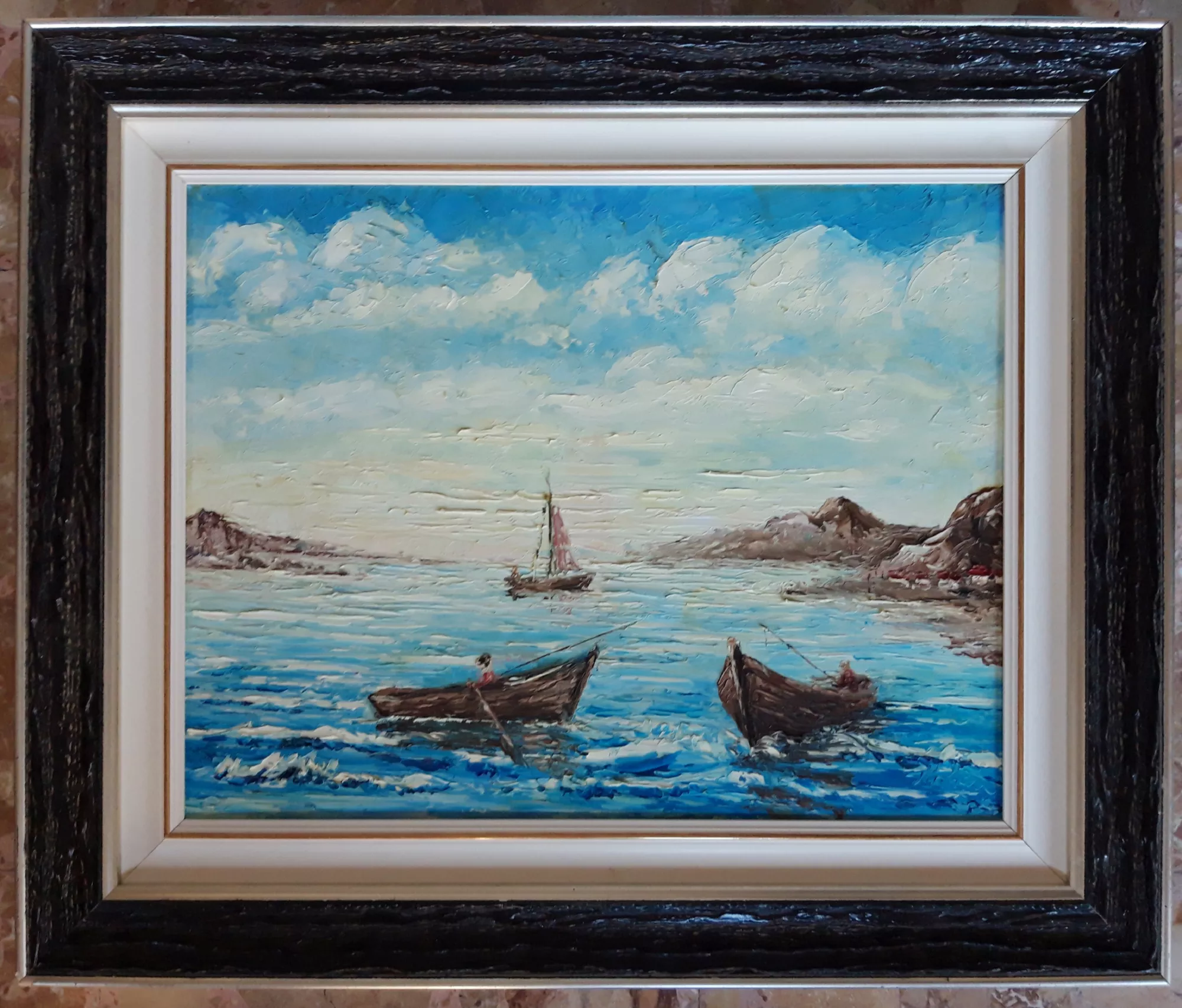 Paesaggio-marino-con-barche-Aly-Mohsen "Quadro di Ay Mohsen realizzato ad Olio con spatola. Il titolo è Paesaggio marino con barche e rientra nella categoria Il mare. Paesaggio marino con barche è un dipinto realizzato con tecnica a spatola in cui Aly Mohsen interpreta la vita sul mare attraverso una pittura materica, intensa e dinamica. In primo piano, due piccole imbarcazioni in legno solcano le acque increspate, costruite con spessi impasti di colore che restituiscono movimento e profondità alla superficie marina. Le figure a bordo, appena accennate, suggeriscono una scena quotidiana legata al lavoro, all’attesa e al silenzio del paesaggio costiero. Al centro della composizione, una barca a vela più distante accompagna lo sguardo verso l’orizzonte, creando un equilibrio visivo armonioso tra primo piano e sfondo. Le coste rocciose che delimitano la scena rafforzano la struttura compositiva e guidano visivamente l’apertura verso il mare aperto, ampliando la percezione dello spazio. Il cielo, ampio e luminoso, è costruito attraverso sovrapposizioni materiche di azzurri e bianchi che enfatizzano la sensazione di aria, luce e profondità atmosferica. La cornice, caratterizzata da toni scuri all’esterno e chiari all’interno, dialoga con i contrasti cromatici del dipinto e valorizza l’intensità materica della pittura, contribuendo all’equilibrio complessivo dell’opera."
