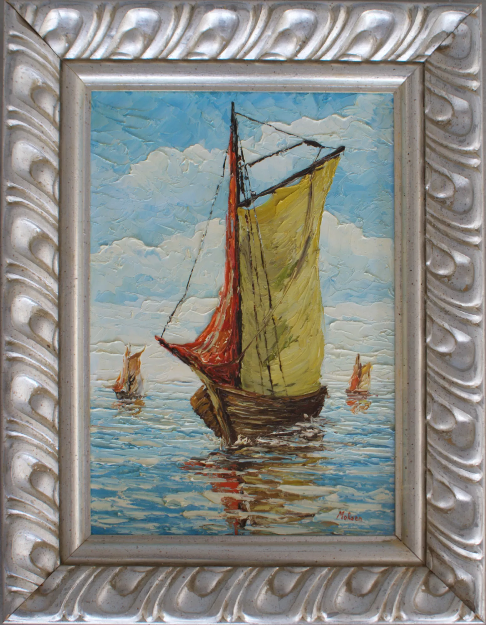 Barca-con-due-barche-piccole-sullo sfondo-Aly-Mohsen "Quadro di Ay Mohsen realizzato ad Olio con spatola. Il titolo è Barca con due barche piccole sullo sfondo e rientra nella categoria Il mare. Opera originale di Aly Mohsen raffigurante una barca a vela tradizionale in primo piano, colta mentre avanza lentamente su un mare calmo, con due imbarcazioni più piccole sullo sfondo che ampliano la profondità della scena e rafforzano il senso di spazio e distanza. Il dipinto è realizzato a olio su tela con tecnica a spatola, elemento centrale della ricerca pittorica dell’artista, che conferisce alla superficie una marcata matericità e una vibrante resa luminosa. La composizione è costruita sul dialogo cromatico tra la vela giallo-ocra e la vela rossa laterale, che emergono con forza sullo sfondo degli azzurri e dei blu del mare e del cielo. Le spatolate decise e sovrapposte modellano un’acqua viva e riflettente, nella quale la barca si specchia creando giochi di luce e movimento. Il cielo, anch’esso lavorato a spatola, presenta nuvole morbide e dinamiche che contribuiscono a un’atmosfera serena, ma visivamente intensa. Il soggetto, essenziale e fortemente evocativo, richiama temi universali come il viaggio, la libertà e la tradizione marinara mediterranea, elementi ricorrenti nella produzione figurativa di Aly Mohsen. La presenza delle barche sullo sfondo introduce un equilibrio compositivo e una dimensione narrativa che arricchisce la lettura dell’opera. Il dipinto è completato da una cornice argentata finemente lavorata, caratterizzata da motivi classici in rilievo, che incornicia l’opera con eleganza e solidità, valorizzando la luminosità dei colori e l’intensità della materia pittorica."