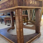 "Opera di Aly Mohsen realizzata con la tecnica dell'intarsio. Il titolo è Scrivania delle chimere e rientra nella categoria Ebanisteria Monumentale. La Scrivania delle Chimere è un’opera di ebanisteria artistica monumentale di Aly Mohsen, concepita come pezzo unico e realizzata secondo i principi della grande tradizione europea dell’alta falegnameria d’arte. L’opera si colloca al confine tra scultura funzionale e manufatto simbolico, integrando architettura, decorazione e iconografia in una struttura coerente e unitaria. Il piano è realizzato in radica di noce selezionata, caratterizzata da una venatura complessa e simmetrica, valorizzata da una finitura accurata che ne esalta la profondità cromatica e la qualità materica. La superficie è incorniciata da un intarsio policromo composto da acero bianco, ebano e padouk, disposto secondo un disegno continuo di gusto classico, eseguito con elevata precisione tecnica. La struttura portante è in mogano massello, utilizzato per le gambe, le fasce e gli elementi architettonici principali. Le superfici verticali sono arricchite da intarsi in acero bianco, interamente realizzati a mano, con motivi ornamentali e figurativi che dialogano con la struttura senza sovraccaricarla. La base inferiore curva e il collegamento tra le gambe contribuiscono alla stabilità visiva e strutturale dell’insieme. Elemento distintivo dell’opera è la presenza delle chimere alate intarsiate lungo le fasce laterali. Queste figure assumono un valore iconografico e simbolico, richiamando temi di protezione, forza e trasformazione, ricorrenti nella ricerca artistica di Mohsen. L’inserimento delle chimere non è puramente decorativo, ma parte integrante della concezione narrativa e formale dell’opera. La scrivania è concepita come opera d’arte funzionale, in cui l’uso pratico è subordinato a una visione artistica complessiva. La qualità dei materiali, la lavorazione manuale e l’unità tra struttura e decorazione ne fanno un manufatto destinato a contesti rappresentativi, in cui possa essere letto e osservato come oggetto artistico autonomo."