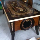"Opera di Ay Mohsen realizzata con la tecnica dell'intarsio. Il titolo è Scrivania del poker e le tre carte e rientra nella categoria Ebanisteria Monumentale. Questa imponente scrivania monumentale rappresenta una delle opere più concettualmente audaci, raffinate e politicamente consapevoli di Aly Mohsen. In essa, la grande tradizione dell’ebanisteria artistica europea viene trasformata in strumento narrativo, simbolico e apertamente critico, dando vita a un’opera che trascende la funzione d’arredo per assumere la forma di messaggio cifrato e denuncia silenziosa. Non si tratta di un semplice mobile funzionale, ma di una vera opera d’arte tridimensionale, concepita per dialogare con il potere, smascherarne i meccanismi e mettere in crisi le apparenze di legalità e correttezza. Struttura e materiali La scrivania è caratterizzata da una struttura solida ma visivamente equilibrata, con gambe sagomate e slanciate che alleggeriscono la massa monumentale del piano. L’opera è realizzata con una selezione estremamente ricercata di legni pregiati, scelti non solo per le qualità estetiche ma anche per il loro valore simbolico: Noce nazionale e noce canaletto per la struttura principale e le superfici estese, apprezzati per la profondità cromatica e la stabilità nel tempo Radica di noce per i pannelli frontali, impiegata per ottenere superfici vibranti e irregolari, metafora visiva dell’instabilità e dell’inganno Ebano ed essenze scure tinte per i fondi degli intarsi, funzionali a rafforzare il contrasto grafico Acero e acero sicomoro per gli intarsi chiari Legni naturalmente colorati (padouk, acero, mogano, rovere, radica di noce, ebano verde ed ebano nero) per la resa cromatica delle figure e delle carte da gioco Il bordo chiaro e continuo del piano richiama deliberatamente la tradizione dei grandi tavoli da gioco, incorniciando la scena e convogliando lo sguardo verso il centro narrativo. Il piano: il gioco come metafora del potere Il piano superiore costituisce il cuore concettuale dell’opera. All’interno di una ricchissima cornice ornamentale intarsiata si sviluppa una sequenza di carte da poker disposte con apparente casualità. A una prima lettura, l’immagine suggerisce una partita in corso. A uno sguardo più attento, emerge però un elemento perturbante: le combinazioni non conducono a nessun esito logico. Le mani sono incoerenti, impossibili, volutamente manipolate. Questa ambiguità è intenzionale. Il poker, simbolo di strategia, calcolo e rischio controllato, viene qui messo in relazione con il gioco delle tre carte, archetipo universale della truffa. Il messaggio è sottile ma inequivocabile: chi crede di giocare secondo regole condivise è già vittima di un inganno. Il fronte: musica, scena e finzione Il fronte della scrivania è dominato da un grande medaglione circolare intarsiato, nel quale compaiono strumenti musicali, spartiti, carte da gioco e motivi floreali. La musica diventa metafora della messa in scena del potere: un concerto apparentemente armonioso che nasconde dissonanze profonde, una composizione elegante pensata per distrarre, sedurre e confondere. Le fasce laterali, ornate con ghirlande classiche e figure stilizzate, richiamano consapevolmente il linguaggio neoclassico e ottocentesco, rafforzando l’idea di ordine, autorità e rispettabilità — un ordine solo apparente. Storia dell’opera e valore simbolico La scrivania fu commissionata da un importante uomo d’affari egiziano, figura di enorme peso economico internazionale. Aly Mohsen, che conosceva il committente fin dall’infanzia, aveva fondati motivi per ritenere che questi operasse in realtà come prestanome per i servizi segreti statunitensi, coinvolto in operazioni economiche e finanziarie condotte in Italia. Al momento della consegna, Mohsen si recò personalmente nell’ufficio del committente e ne spiegò il significato con parole che rivelano la natura profonda dell’opera: «Questa scrivania serve per avvisare chi si siede di fronte a te: lui pensa di giocare a poker, mentre tu stai giocando al gioco delle tre carte.» Un’accusa di straordinaria eleganza, affidata non al linguaggio diretto ma alla forza simbolica dell’intarsio. Il committente, comprendendo perfettamente il messaggio, si sentì apertamente insultato e rifiutò l’opera. La scrivania rimase così nelle mani dell’artista. Rimasta nella disponibilità dell’artista, la Scrivania del Poker e del Gioco delle Tre Carte possiede oggi un valore ulteriormente accresciuto. È un pezzo unico, documentato, con una storia forte, verificabile e di straordinaria attrattiva per il collezionismo internazionale. L’opera unisce: alta ebanisteria artistica contenuto politico e narrativo qualità museale dimensioni monumentali provenienza diretta dall’artista Per collezionisti evoluti e investitori in mobili d’arte, arti decorative e opere concettuali, questa scrivania rappresenta un caso raro di arredo che diventa linguaggio critico, capace di dialogare con design, scultura e arte contemporanea, e destinato a una progressiva valorizzazione culturale e patrimoniale. In Aly Mohsen, il legno non è mai solo materia: diventa linguaggio, accusa, ironia e memoria. E questa scrivania ne è una delle dichiarazioni più lucide e implacabili."