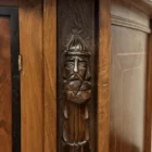 "Opera di Ay Mohsen realizzata con la tecnica dell'intarsio. Il titolo è Credenza del ponte vecchio e rientra nella categoria Ebanisteria Monumentale. La Credenza del Ponte Vecchio di Ivrea è un mobile artistico intarsiato e scolpito concepito come opera unica di alta ebanisteria, nel quale confluiscono tradizione figurativa, lavorazione lignea d’autore e riferimento paesaggistico di carattere identitario. L’opera si configura come un manufatto tridimensionale complesso, in cui struttura architettonica, decorazione plastica e apparato intarsiato concorrono alla definizione di un insieme unitario. La struttura è realizzata in mogano massello e radica di noce, utilizzati per le parti portanti e per le superfici principali, con un’alternanza di campiture compatte e venature irregolari che articolano il volume complessivo. Le fiancate presentano elementi scultorei in noce, interamente scolpiti a mano, raffiguranti figure stilizzate integrate verticalmente nei montanti, che accentuano il carattere plastico e monumentale del mobile e richiamano la tradizione europea dell’intaglio figurativo. Il bordo superiore e il cassetto sono realizzati in ebano, introducendo un contrasto cromatico netto con le essenze più calde della struttura. Le ante superiori presentano fondi scuri in ebano sui quali si sviluppano intarsi floreali policromi, eseguiti in acero, noce, ebano verde e ciliegio, organizzati in composizioni simmetriche che definiscono un equilibrio tra decorazione e ordine geometrico. Elemento centrale dell’opera è il grande pannello intarsiato posto nella parte inferiore del mobile, raffigurante una veduta del Ponte Vecchio di Ivrea. La scena paesaggistica è costruita mediante una complessa combinazione di essenze lignee, tra cui acero, radica di noce, noce chiaro e scuro ed ebano verde, utilizzate per ottenere variazioni tonali, profondità spaziale e articolazione luministica. Il riquadro è delimitato da una cornice in legno di rose che ne definisce il perimetro e ne isola visivamente l’immagine dal resto della struttura. L’interno del mobile è completamente rifinito e decorato, con pannelli intarsiati a motivi floreali e superfici arricchite da disegni geometrici a raggiera e campiture angolari ottenute mediante l’accostamento di diverse essenze lignee. Le decorazioni interne sono concepite come parte integrante dell’opera e risultano pienamente visibili grazie alla presenza di un ripiano in vetro, che consente la lettura continua degli intarsi anche a mobile aperto. La credenza si conclude con una cornice strutturale continua che accompagna i profili superiori e inferiori del mobile, realizzata in essenza scura con finitura uniforme, avente la funzione di contenere visivamente il volume complessivo e di raccordare le diverse superfici lignee in un insieme coerente e unitario."