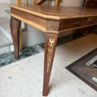 "Opera di Ay Mohsen realizzato con la tecnica dell'intarsio. Il titolo è Scrivania neoclassica e rientra nella categoria Ebanisteria Monumentale. Questa scrivania neoclassica intarsiata di Aly Mohsen si configura come opera di alta ebanisteria artistica, concepita come manufatto unitario in cui funzione e costruzione formale sono integrate in una struttura di carattere decorativo e architettonico. L’opera si colloca nel solco della tradizione dell’arredo classico europeo, riletta attraverso un controllo rigoroso dei materiali e della composizione. Il piano è realizzato in piuma di mogano selezionata, caratterizzata da una venatura simmetrica e continua che definisce una superficie compatta e visivamente coerente. L’area centrale è incorniciata da un articolato sistema di intarsi in acero chiaro, disposti secondo un disegno perimetrale di gusto neoclassico, con motivi floreali e fitomorfi collocati agli angoli e nei punti mediani dei lati. Il rapporto tra la decorazione intarsiata e la marezzatura naturale del mogano è costruito per continuità ritmica e bilanciamento visivo. I bordi del piano sono rifiniti in noce chiaro, introducendo un passaggio cromatico graduale tra superficie e struttura. Il corpo della scrivania e i cassetti sono realizzati in noce scuro, materiale che conferisce solidità visiva e coerenza tonale all’insieme, contribuendo alla lettura architettonica del mobile. Le gambe smontabili sono costruite con un’anima in mogano lamellare, successivamente rivestita in radica di quercia. Su ciascuna gamba sono presenti intarsi verticali in acero chiaro, impostati come elementi ornamentali continui che accentuano lo sviluppo verticale e il carattere scultoreo della struttura. Il bordo perimetrale del piano, trattato come cornice funzionale dell’intera composizione, svolge un ruolo di contenimento visivo e di definizione spaziale dell’opera, delimitando la superficie intarsiata e contribuendo alla stabilità formale e percettiva della scrivania.""Quadro di Ay Mohsen realizzato ad Intarsio. Il titolo è Scrivania neoclassica e rientra nella categoria Ebanisteria Monumentale. Questa scrivania neoclassica intarsiata di Aly Mohsen si configura come opera di alta ebanisteria artistica, concepita come manufatto unitario in cui funzione e costruzione formale sono integrate in una struttura di carattere decorativo e architettonico. L’opera si colloca nel solco della tradizione dell’arredo classico europeo, riletta attraverso un controllo rigoroso dei materiali e della composizione. Il piano è realizzato in piuma di mogano selezionata, caratterizzata da una venatura simmetrica e continua che definisce una superficie compatta e visivamente coerente. L’area centrale è incorniciata da un articolato sistema di intarsi in acero chiaro, disposti secondo un disegno perimetrale di gusto neoclassico, con motivi floreali e fitomorfi collocati agli angoli e nei punti mediani dei lati. Il rapporto tra la decorazione intarsiata e la marezzatura naturale del mogano è costruito per continuità ritmica e bilanciamento visivo. I bordi del piano sono rifiniti in noce chiaro, introducendo un passaggio cromatico graduale tra superficie e struttura. Il corpo della scrivania e i cassetti sono realizzati in noce scuro, materiale che conferisce solidità visiva e coerenza tonale all’insieme, contribuendo alla lettura architettonica del mobile. Le gambe smontabili sono costruite con un’anima in mogano lamellare, successivamente rivestita in radica di quercia. Su ciascuna gamba sono presenti intarsi verticali in acero chiaro, impostati come elementi ornamentali continui che accentuano lo sviluppo verticale e il carattere scultoreo della struttura. Il bordo perimetrale del piano, trattato come cornice funzionale dell’intera composizione, svolge un ruolo di contenimento visivo e di definizione spaziale dell’opera, delimitando la superficie intarsiata e contribuendo alla stabilità formale e percettiva della scrivania.""Quadro di Ay Mohsen realizzato ad Intarsio. Il titolo è Scrivania neoclassica e rientra nella categoria Ebanisteria Monumentale. Questa scrivania neoclassica intarsiata di Aly Mohsen si configura come opera di alta ebanisteria artistica, concepita come manufatto unitario in cui funzione e costruzione formale sono integrate in una struttura di carattere decorativo e architettonico. L’opera si colloca nel solco della tradizione dell’arredo classico europeo, riletta attraverso un controllo rigoroso dei materiali e della composizione. Il piano è realizzato in piuma di mogano selezionata, caratterizzata da una venatura simmetrica e continua che definisce una superficie compatta e visivamente coerente. L’area centrale è incorniciata da un articolato sistema di intarsi in acero chiaro, disposti secondo un disegno perimetrale di gusto neoclassico, con motivi floreali e fitomorfi collocati agli angoli e nei punti mediani dei lati. Il rapporto tra la decorazione intarsiata e la marezzatura naturale del mogano è costruito per continuità ritmica e bilanciamento visivo. I bordi del piano sono rifiniti in noce chiaro, introducendo un passaggio cromatico graduale tra superficie e struttura. Il corpo della scrivania e i cassetti sono realizzati in noce scuro, materiale che conferisce solidità visiva e coerenza tonale all’insieme, contribuendo alla lettura architettonica del mobile. Le gambe smontabili sono costruite con un’anima in mogano lamellare, successivamente rivestita in radica di quercia. Su ciascuna gamba sono presenti intarsi verticali in acero chiaro, impostati come elementi ornamentali continui che accentuano lo sviluppo verticale e il carattere scultoreo della struttura. Il bordo perimetrale del piano, trattato come cornice funzionale dell’intera composizione, svolge un ruolo di contenimento visivo e di definizione spaziale dell’opera, delimitando la superficie intarsiata e contribuendo alla stabilità formale e percettiva della scrivania."